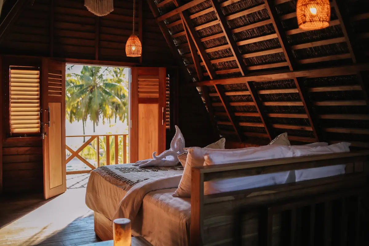 Upstairs king bed under the timber A-frame roof, doors open to the palms
