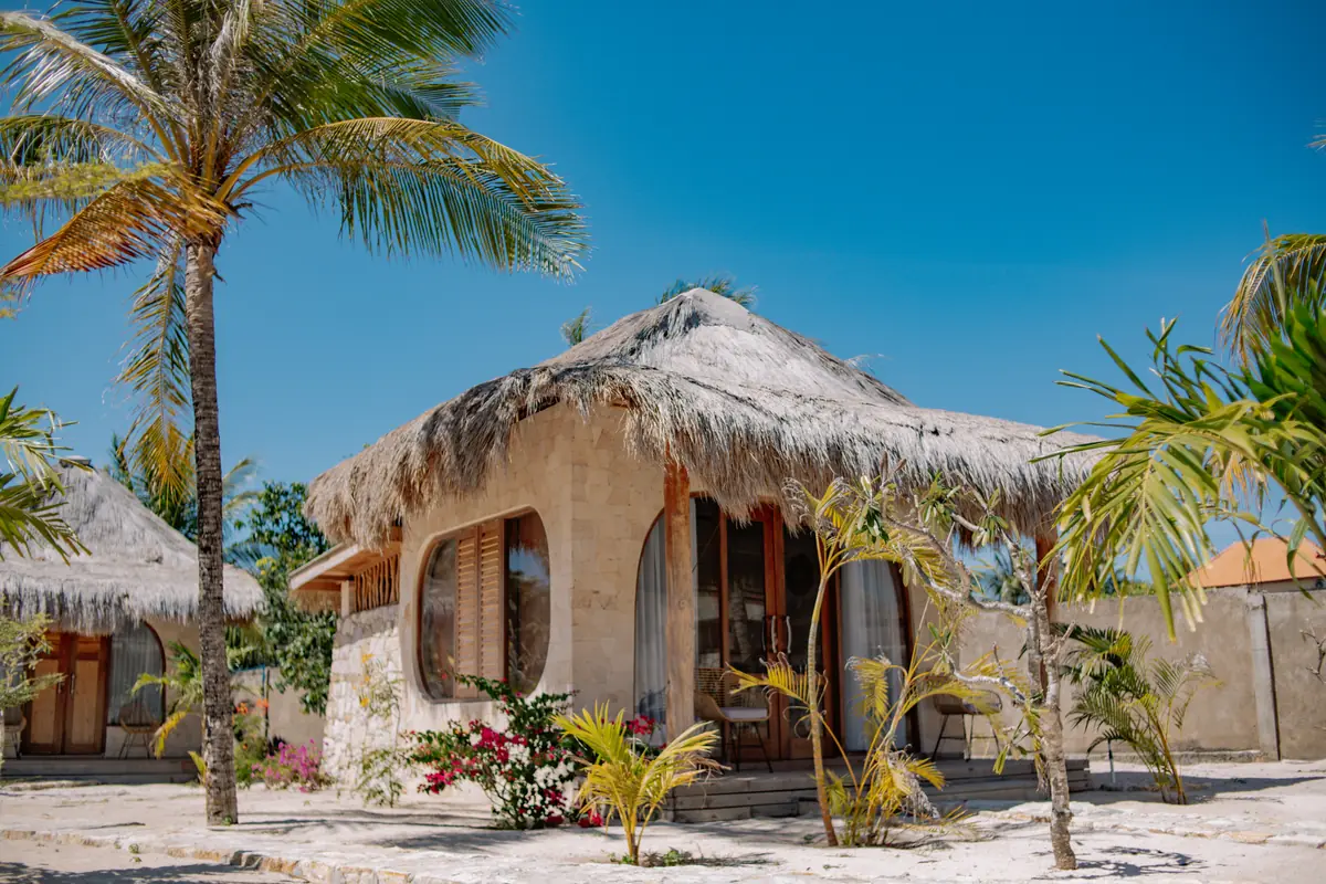 Thatched stone Garden Bungalow among coconut palms under a blue sky