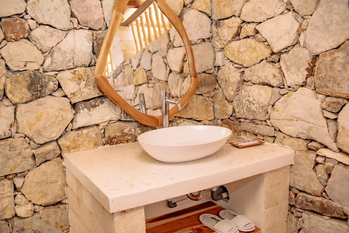 Basin and teak-framed mirror against a hand-laid stone wall