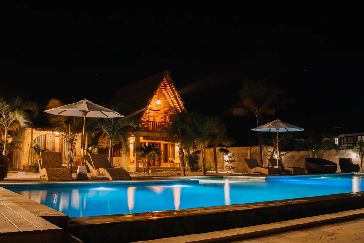 The pool lit blue at night, loungers and umbrellas in front of the glowing Family Room