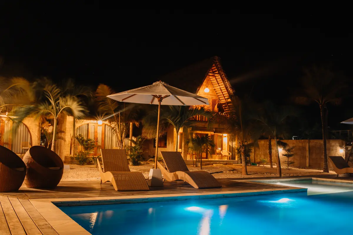 Wicker loungers under an umbrella beside the lit pool