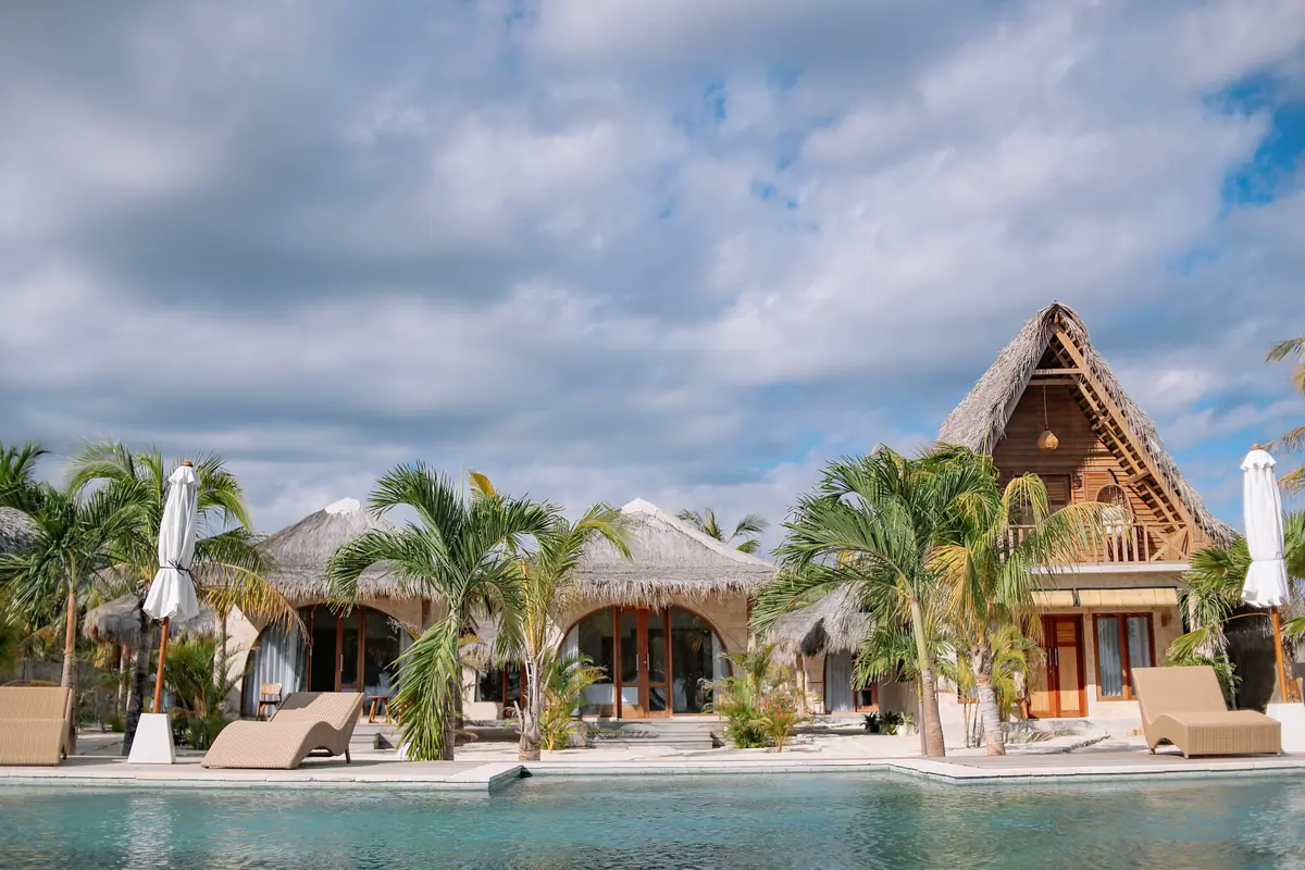 Pool, palms and thatched rooms under a big sky